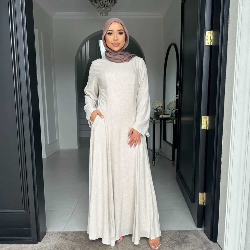Woman in beige modest maxi dress and mauve hijab standing in modern home entryway