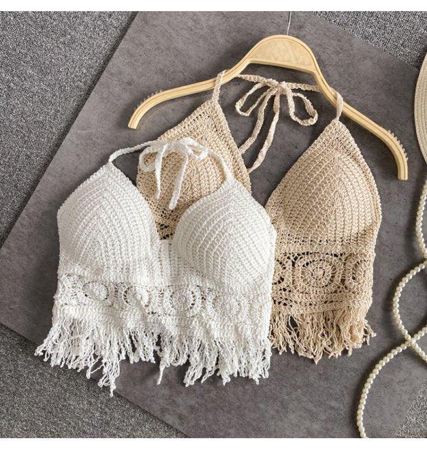 Crochet halter tops in white and beige with fringe detail on wooden hanger on gray surface