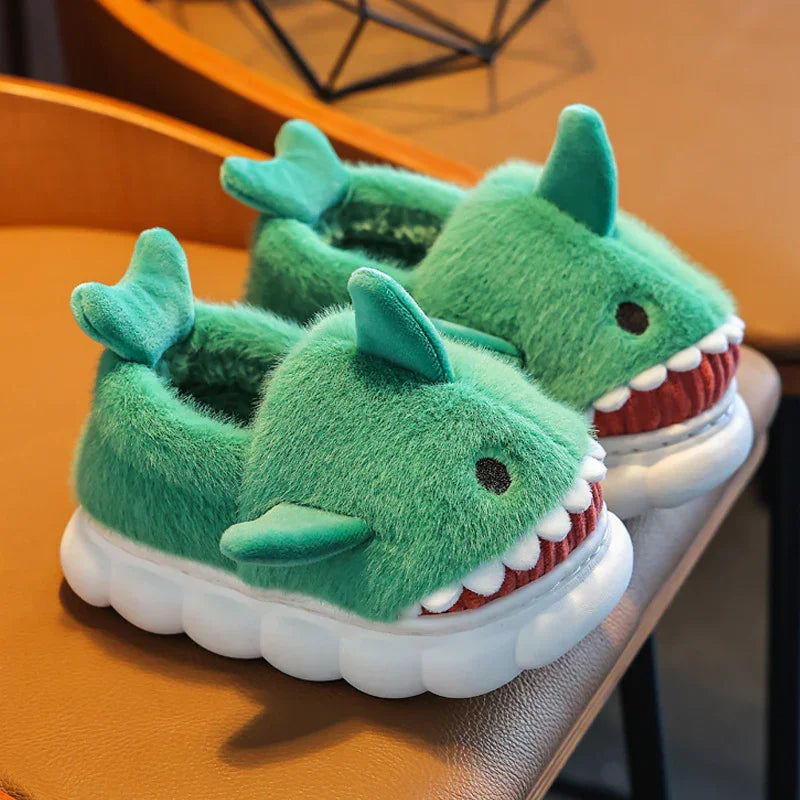 Pair of green plush shark slippers with white teeth and fins on white cushioned soles