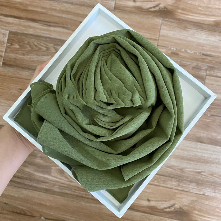 Hand holding white square box with neatly folded olive green fabric inside on wooden floor