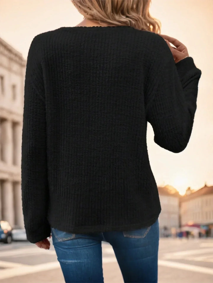 Woman wearing black textured sweater and blue jeans standing outdoors at sunset in urban setting