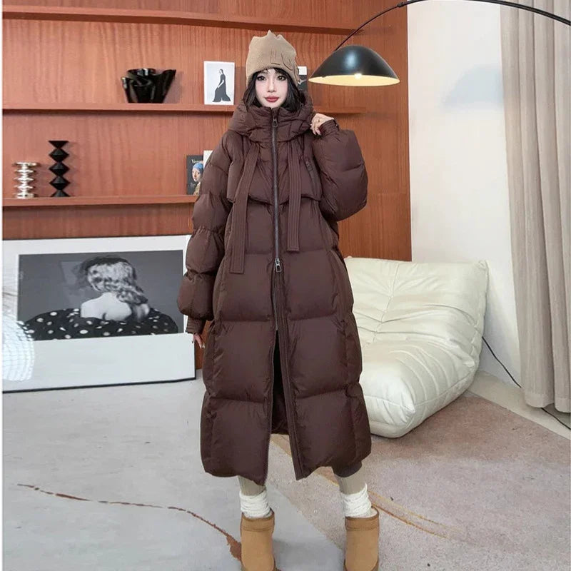 Woman wearing long brown puffer coat with high collar, beige knit hat, and tan boots in modern living room