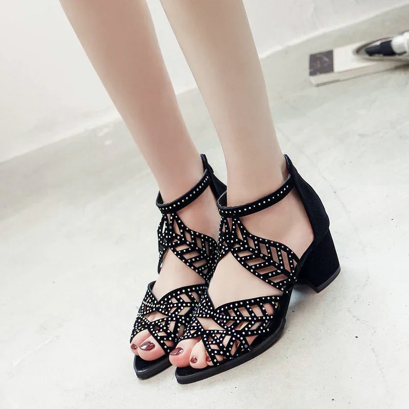 Black strappy block heel sandals with studded leaf pattern on woman's feet, polished nails