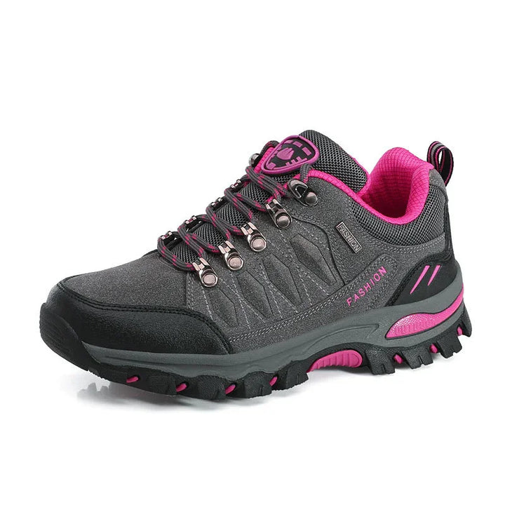 Gray and pink women's hiking shoe with rugged sole and metal eyelets on white background