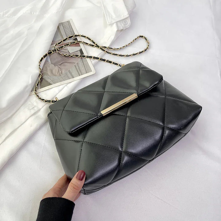 Black quilted leather handbag with gold chain strap and metallic clasp on white fabric background