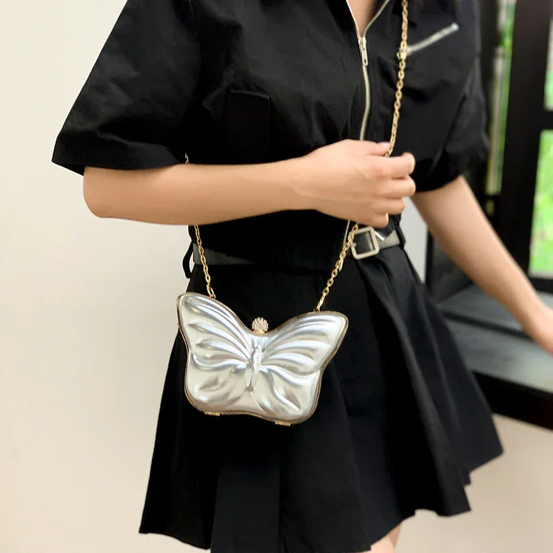 Woman wearing black dress with silver butterfly-shaped purse and gold chain strap