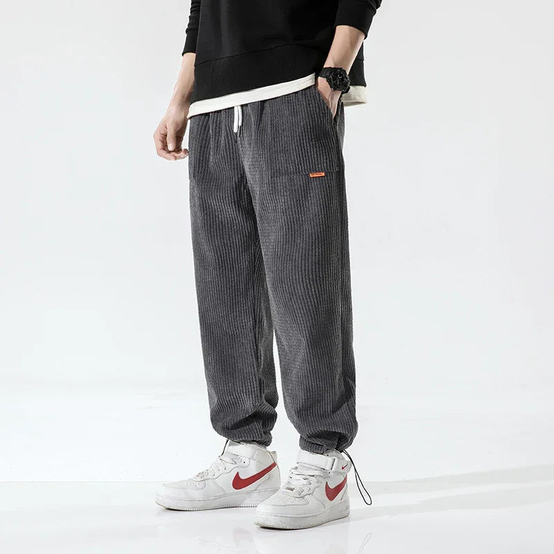Man wearing dark gray corduroy jogger pants with white drawstring and white sneakers with red swoosh