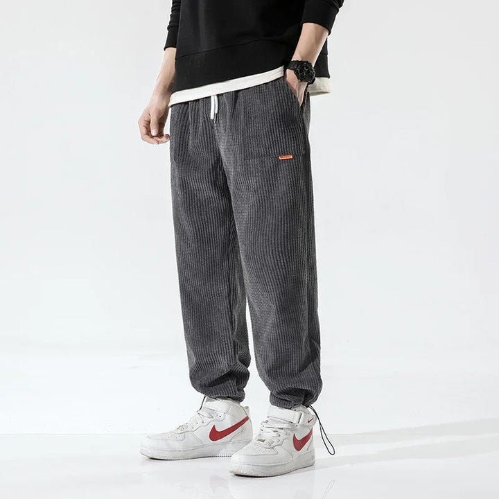 Man wearing dark gray corduroy jogger pants with white drawstring and white sneakers with red swoosh
