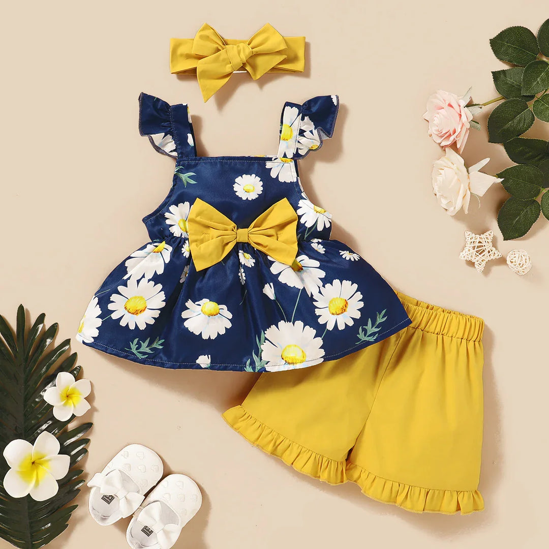Girls summer outfit with navy blue daisy print top, yellow shorts, matching headband, and white shoes