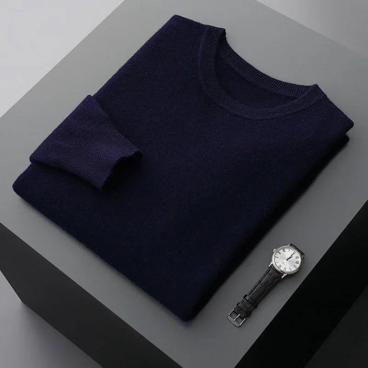 Folded navy blue sweater with one sleeve rolled up next to black leather wristwatch on gray surface