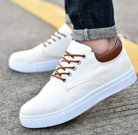 white casual sneakers with brown laces and heel detail worn with rolled-up dark jeans on pavement