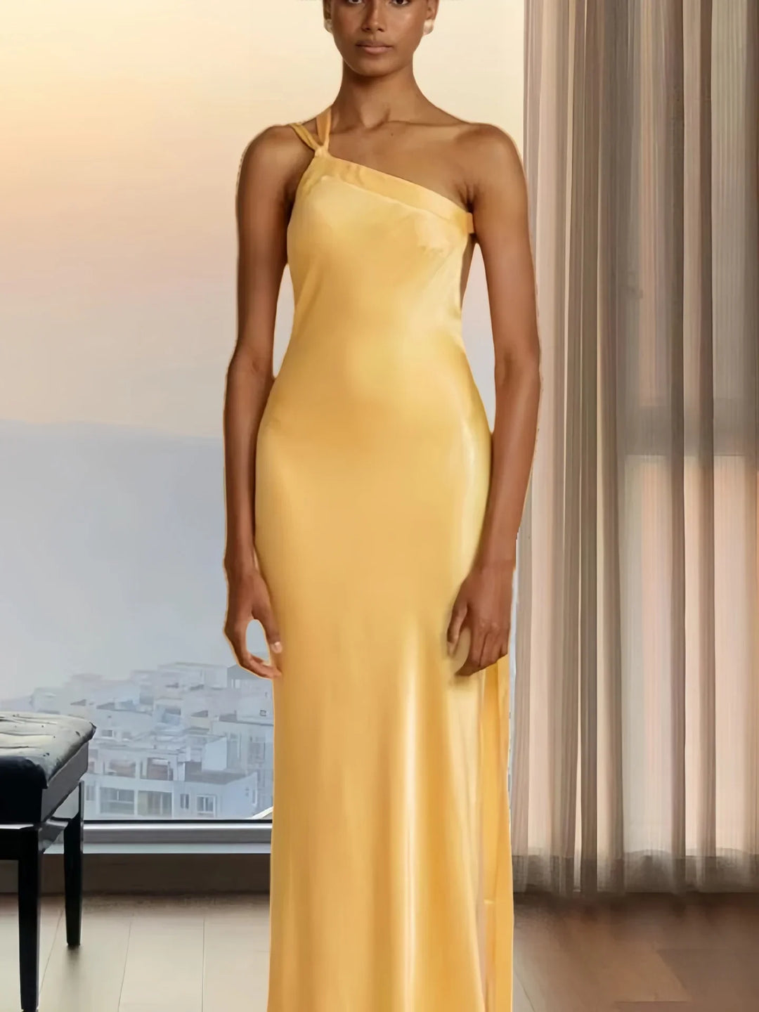Woman wearing a sleek yellow satin one-shoulder evening gown indoors with sheer curtains and window view