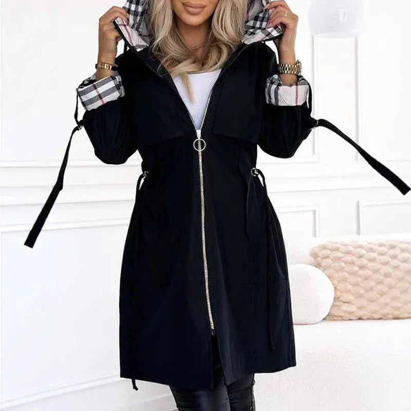 Woman wearing black hooded coat with plaid lining and gold zipper in modern white room