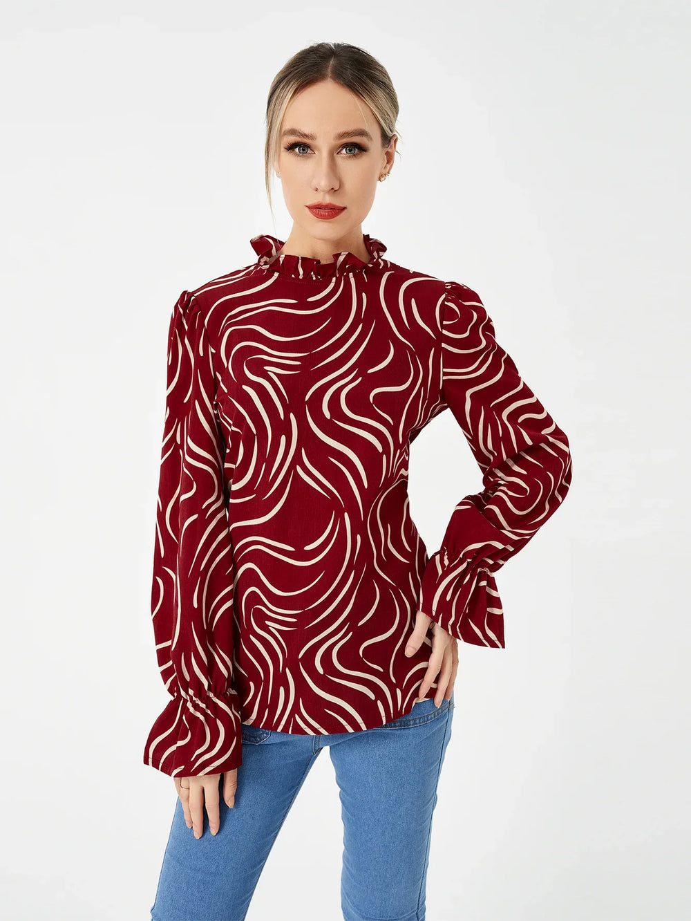 Woman wearing a red blouse with white abstract swirl patterns and ruffled collar and cuffs, paired with blue jeans