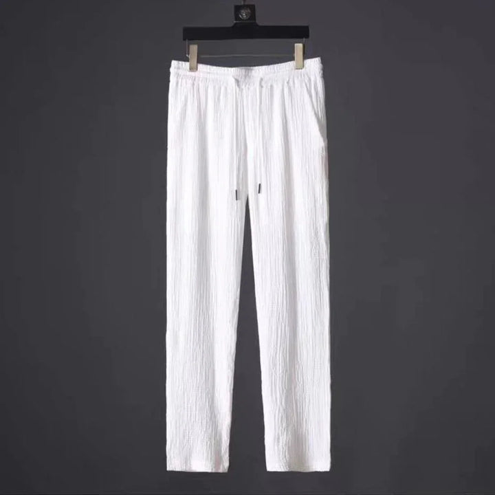 White textured casual pants hanging on black hanger against dark background