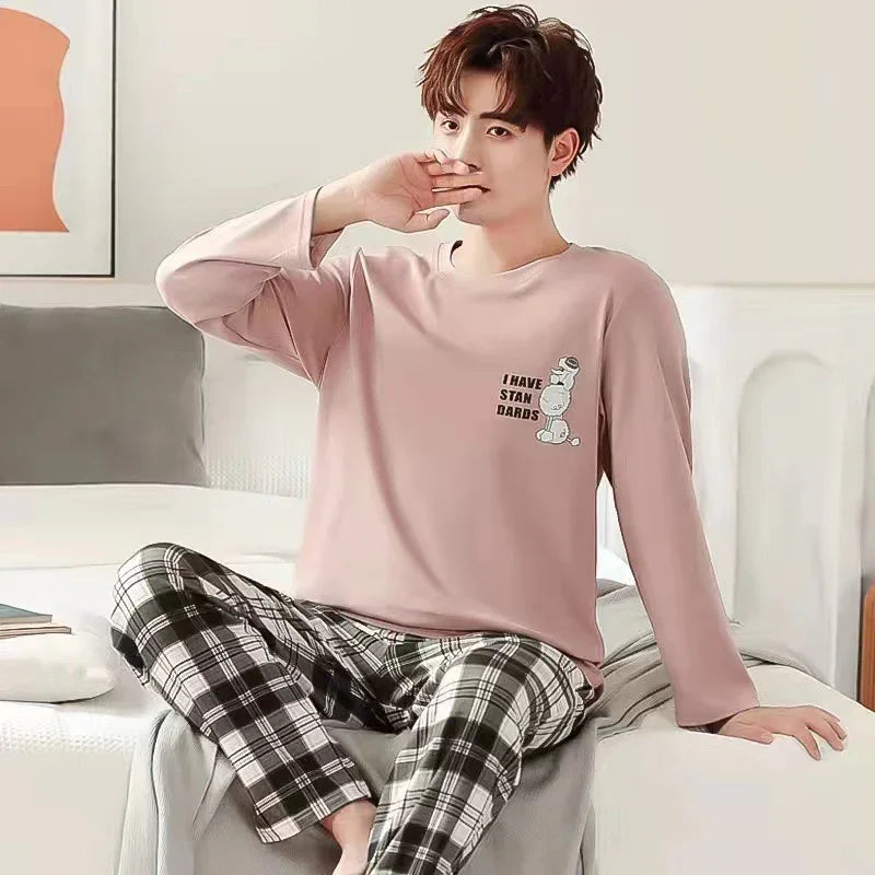 young man in pink long-sleeve pajamas with graphic text sitting on bed in cozy bedroom