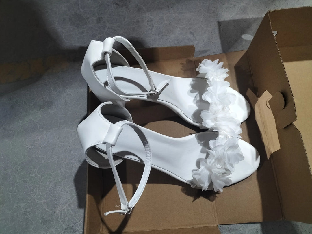 White women's high heel sandals with ankle straps and floral decoration in cardboard box