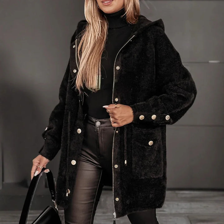 Woman wearing black fuzzy coat with gold buttons, black turtleneck, leather pants, holding black handbag