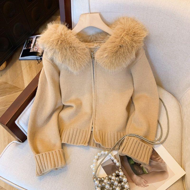 Beige knit cardigan with fluffy fur collar on wooden hanger, pearl chain bag on cream sofa