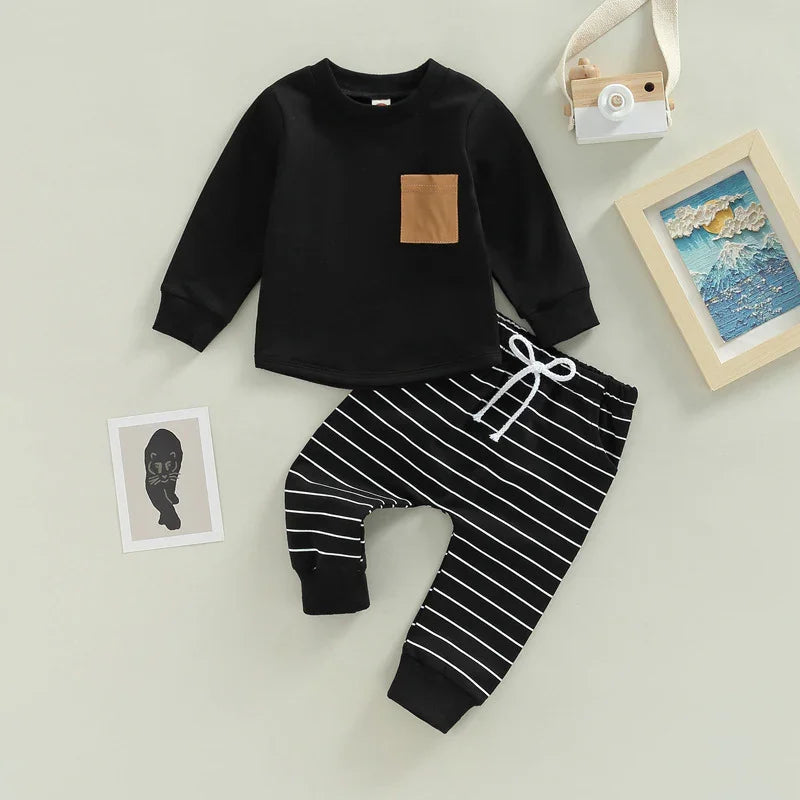 Black long-sleeve toddler shirt with brown pocket and black striped pants with white drawstring on beige background