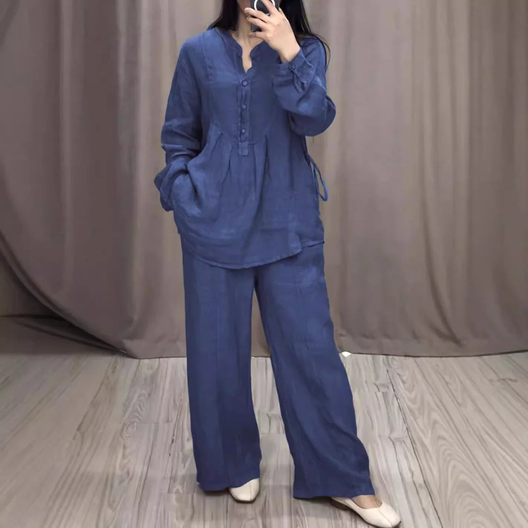 Woman wearing loose blue linen tunic and wide-leg pants with white shoes in a room with wood floor