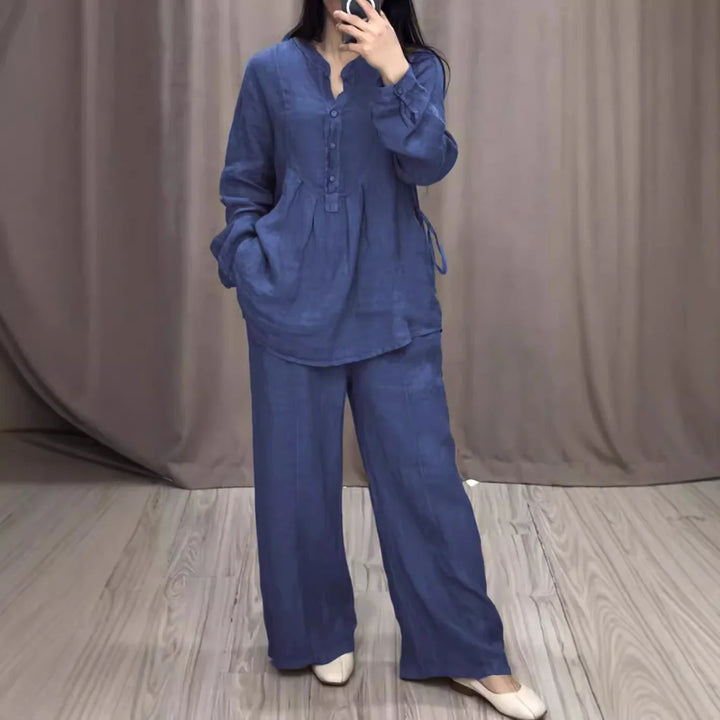 Woman wearing loose blue linen tunic and wide-leg pants with white shoes in a room with wood floor