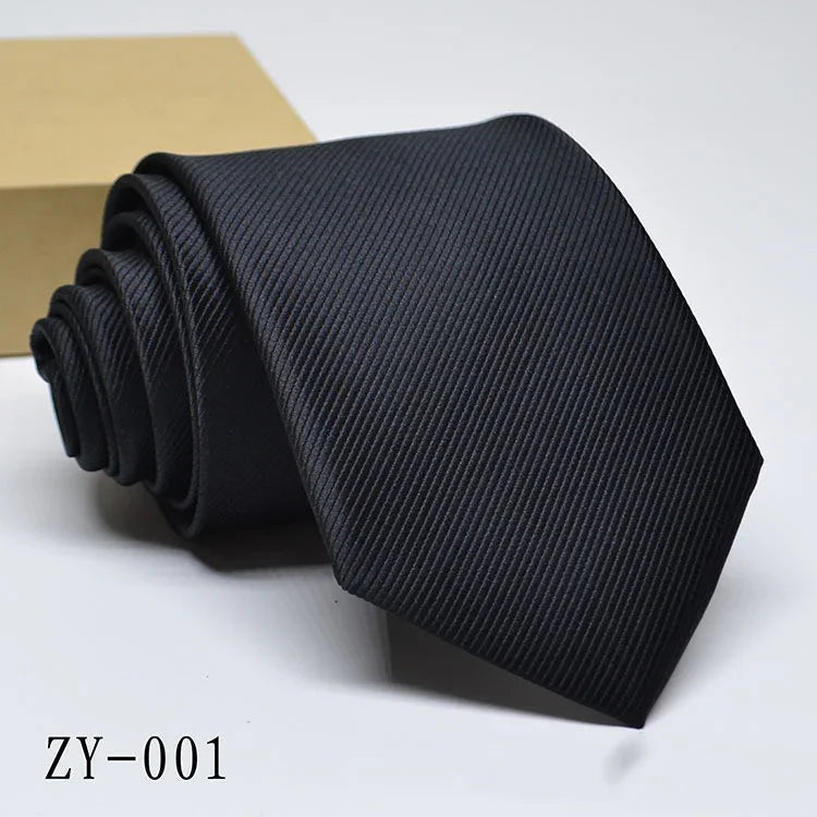 Black textured men's necktie rolled next to a brown box on white background