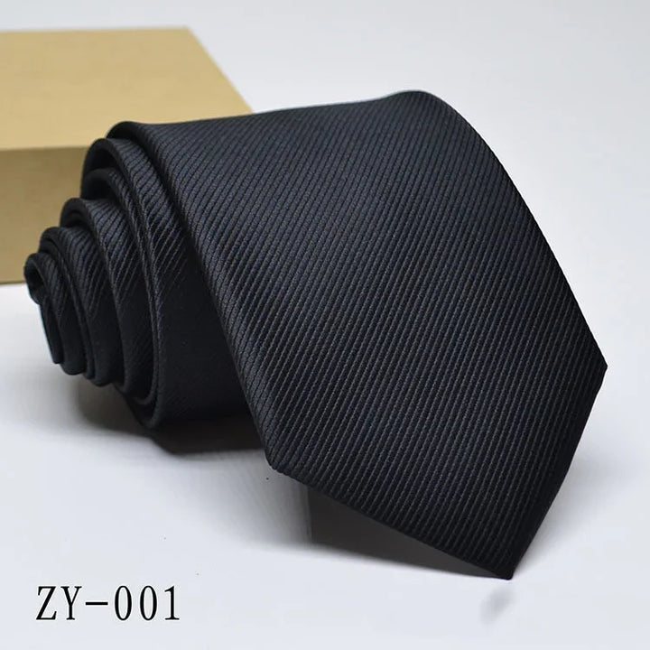Black textured men's necktie rolled next to a brown box on white background