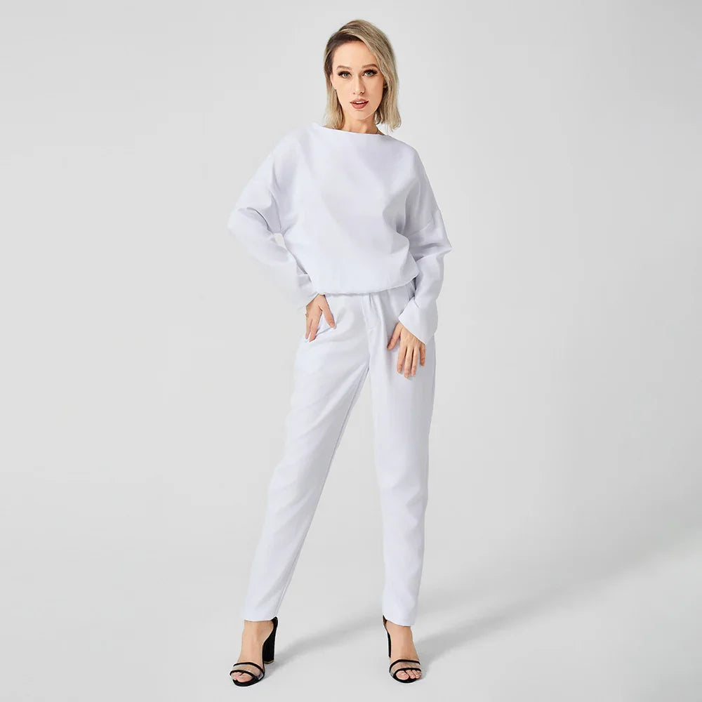 Woman wearing white sweatshirt and pants posing against plain white background in black heels