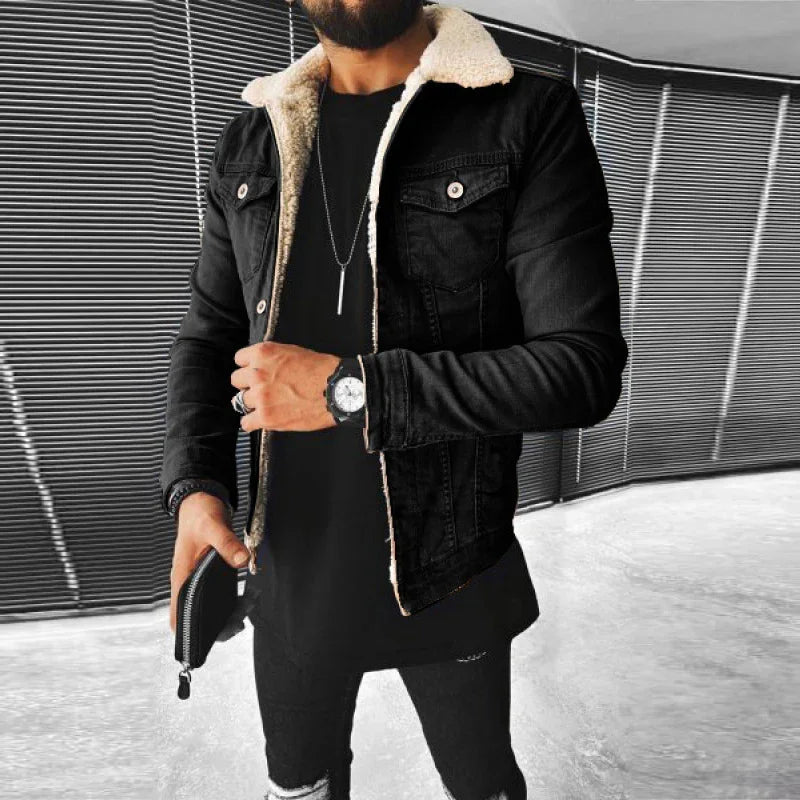 Man wearing black sherpa-lined denim jacket, black ripped jeans, wristwatch, and holding black wallet in modern indoor setting