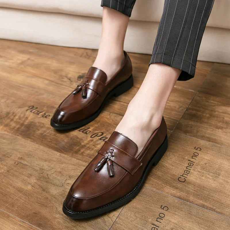 Pair of brown leather tassel loafers worn with pinstriped pants on wooden floor