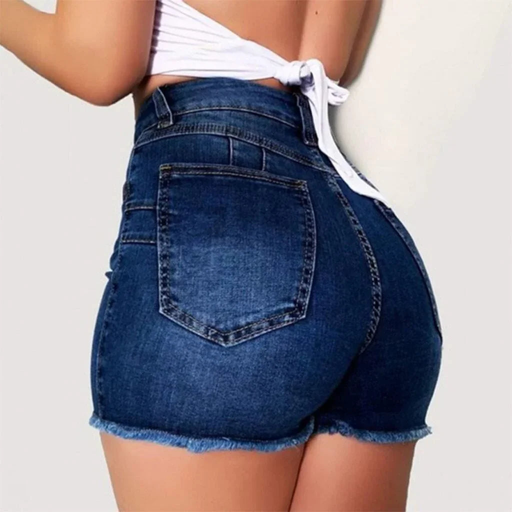 Close-up of woman wearing high-waisted dark blue denim shorts with frayed hems and a white tie-back top
