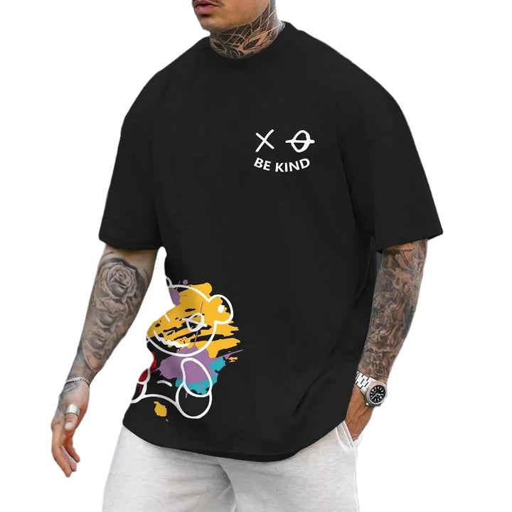 Black short-sleeve t-shirt with white 'Be Kind' text and abstract colorful design worn by tattooed man