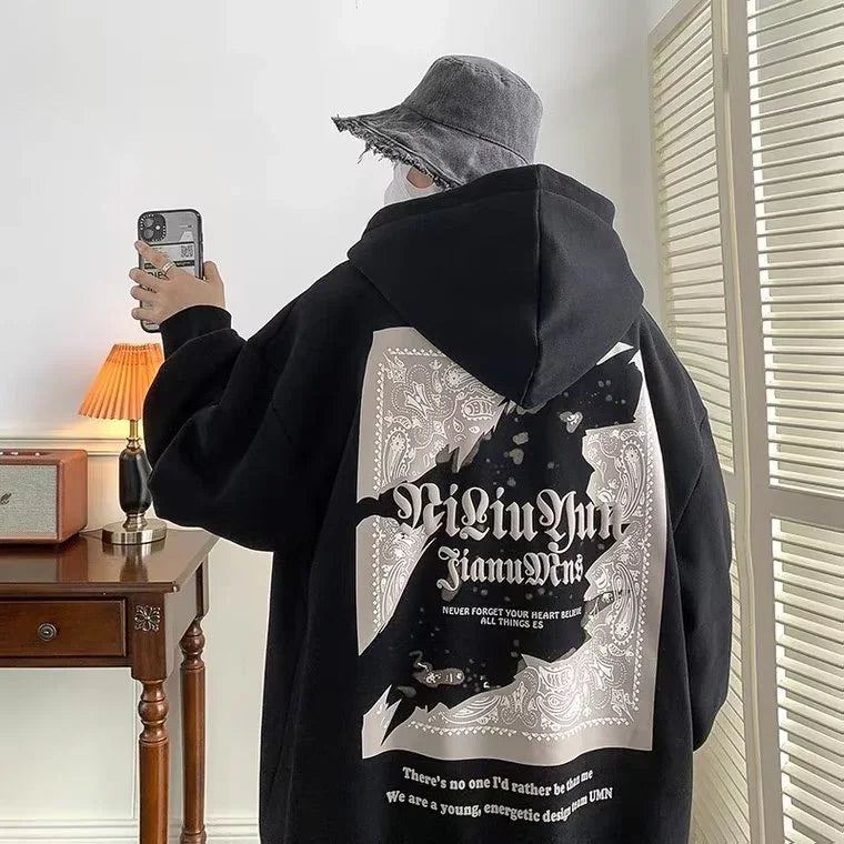 Person wearing black oversized hoodie with graphic bat design and text, gray bucket hat, taking selfie indoors