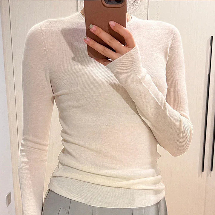 Person wearing a fitted beige long-sleeve ribbed top, taking a mirror selfie with a brown smartphone