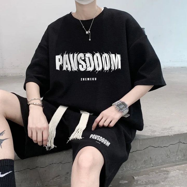 Person wearing black PAWSDOOM brand oversized t-shirt and matching shorts sitting on concrete steps