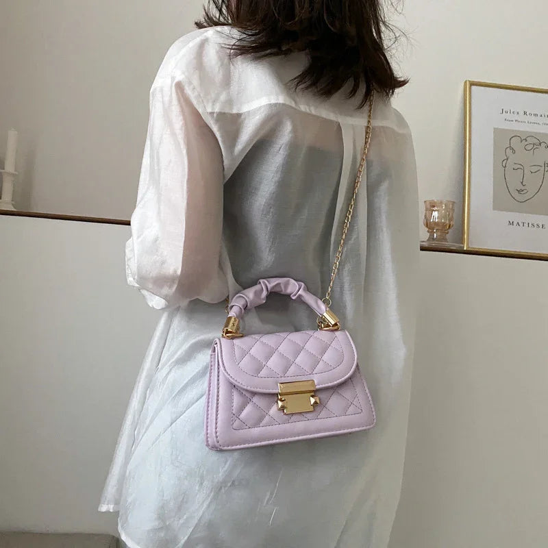 Woman wearing sheer white blouse carrying a lavender quilted handbag with gold chain strap indoors