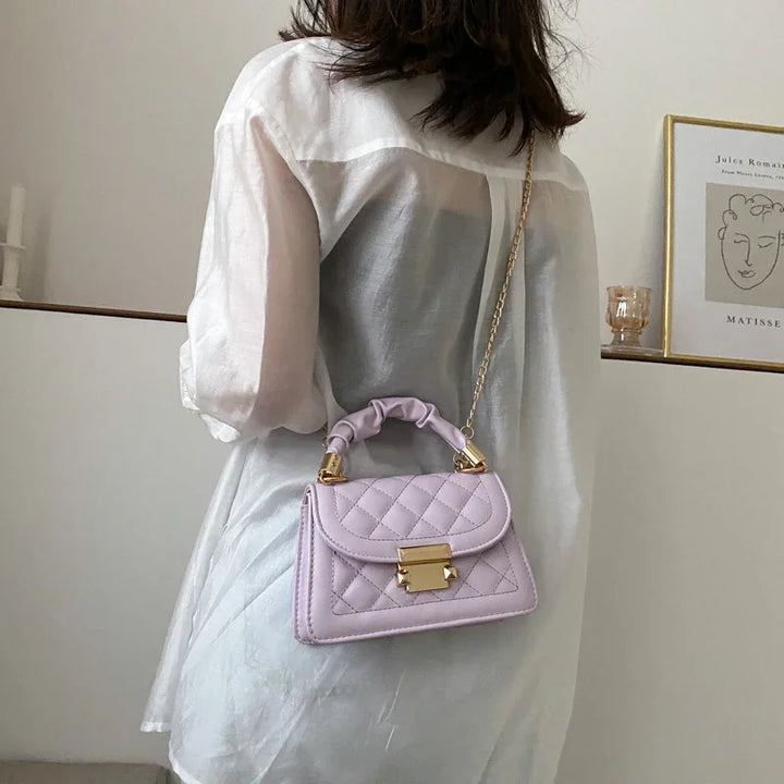 Woman wearing sheer white blouse carrying a lavender quilted handbag with gold chain strap indoors