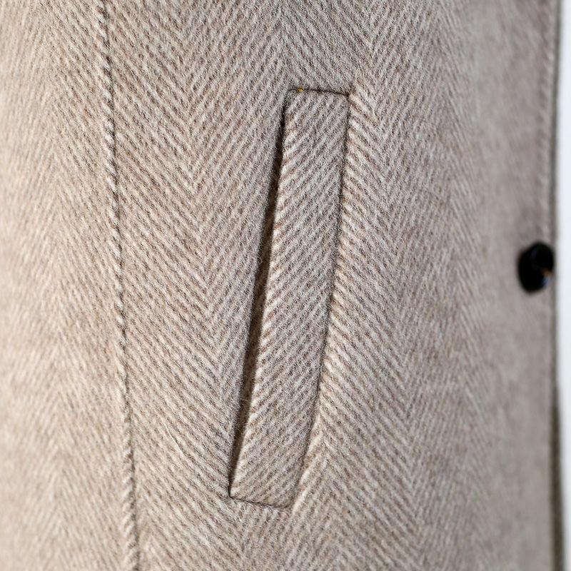 Close-up of beige herringbone wool coat pocket and stitching detail with black button