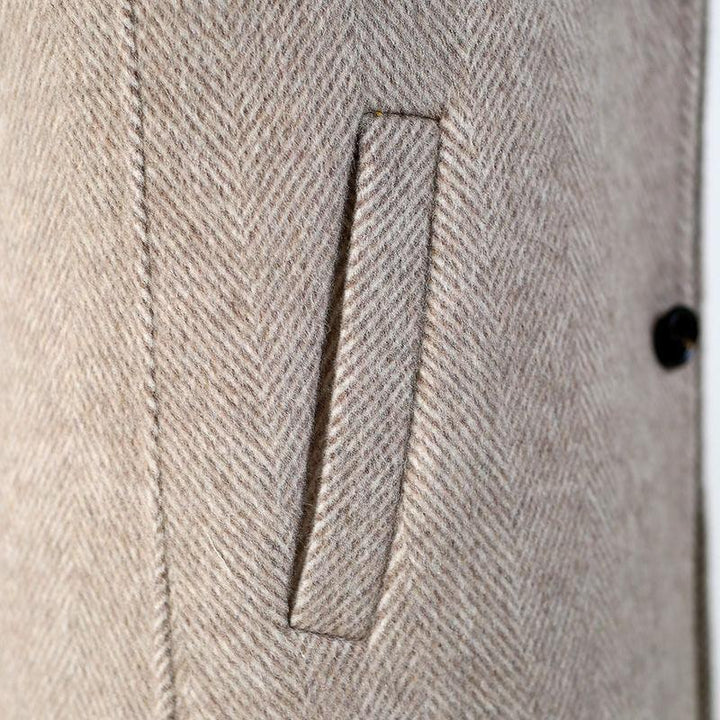 Close-up of beige herringbone wool coat pocket and stitching detail with black button