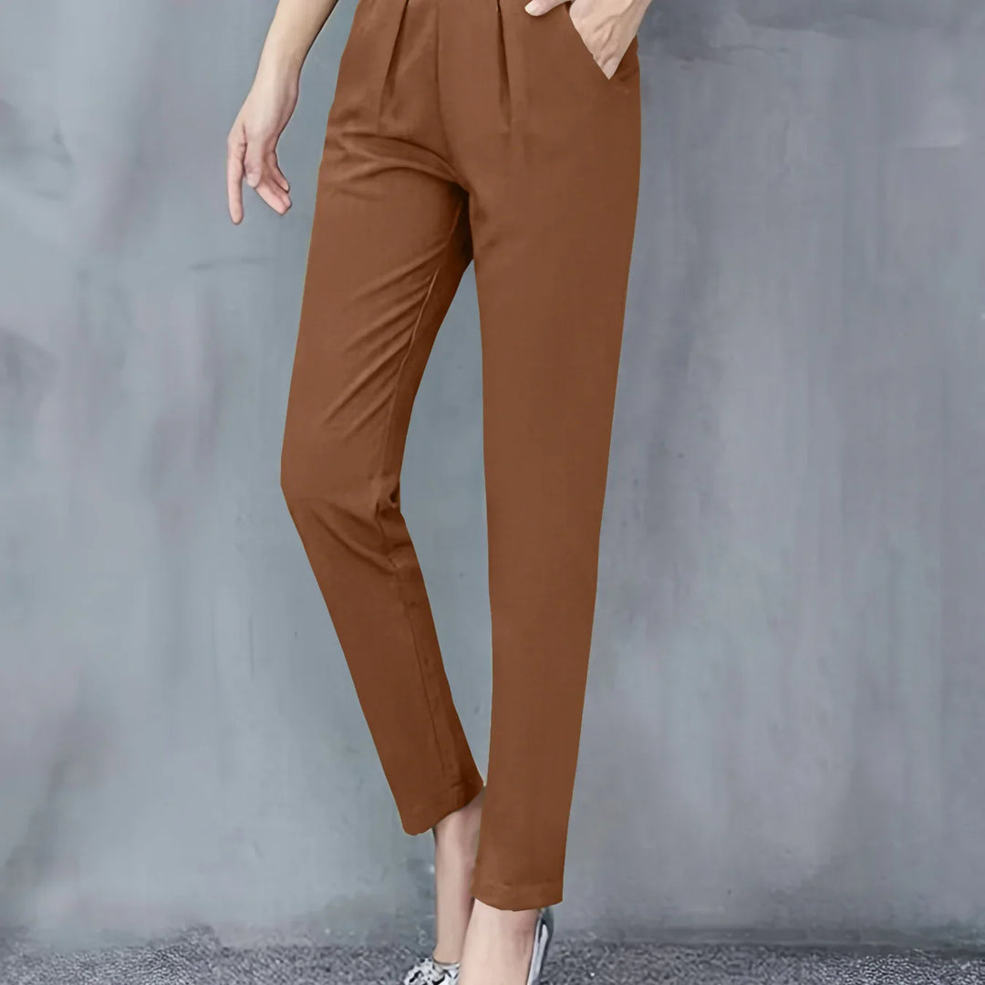 Woman wearing brown slim-fit trousers standing against a gray wall