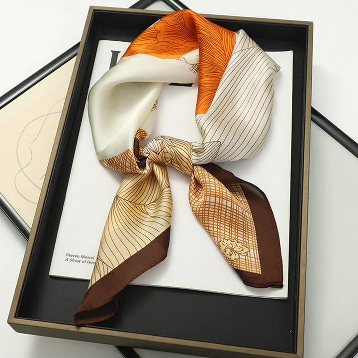 Knotted silk scarf with orange, brown, and beige geometric patterns displayed in black gift box