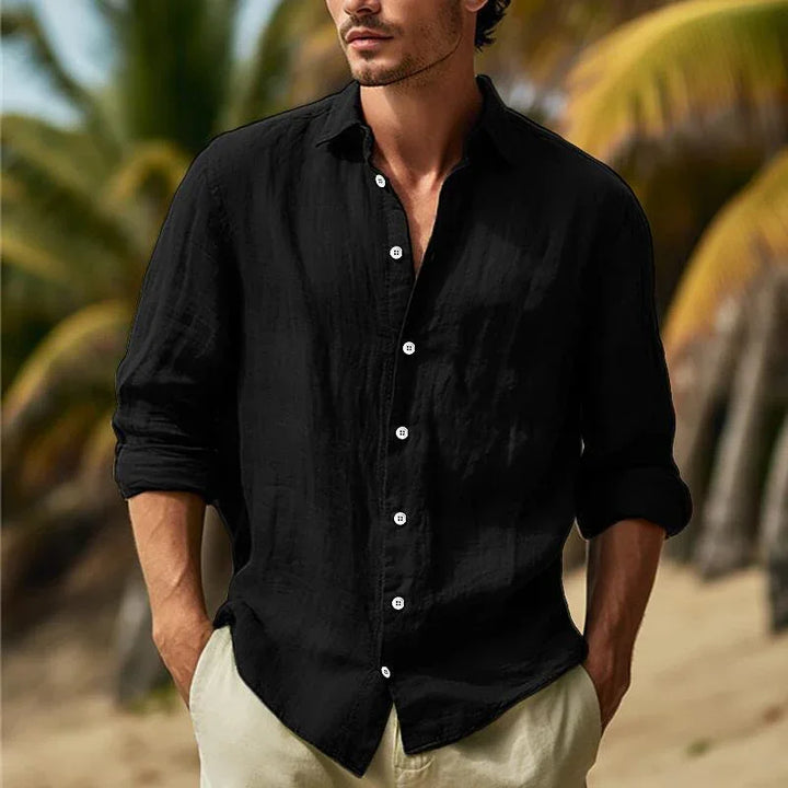 Man wearing black long-sleeve linen shirt with white buttons and beige pants on a tropical beach