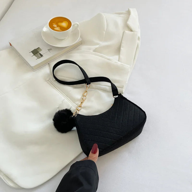 Black quilted handbag with gold chain and pom pom on white blazer and book with coffee cup