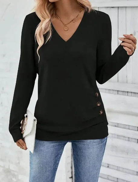 Woman wearing black V-neck long sleeve top with side buttons paired with blue jeans and holding a white clutch