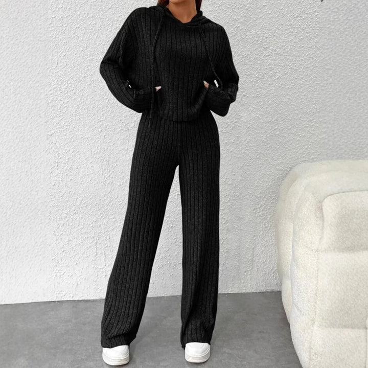 Woman wearing black ribbed knit hoodie and wide-leg pants outfit with white sneakers indoors