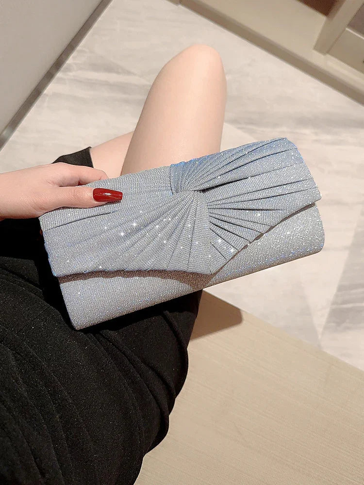 Hand holding silver glittery clutch purse with pleated design on lap wearing black skirt