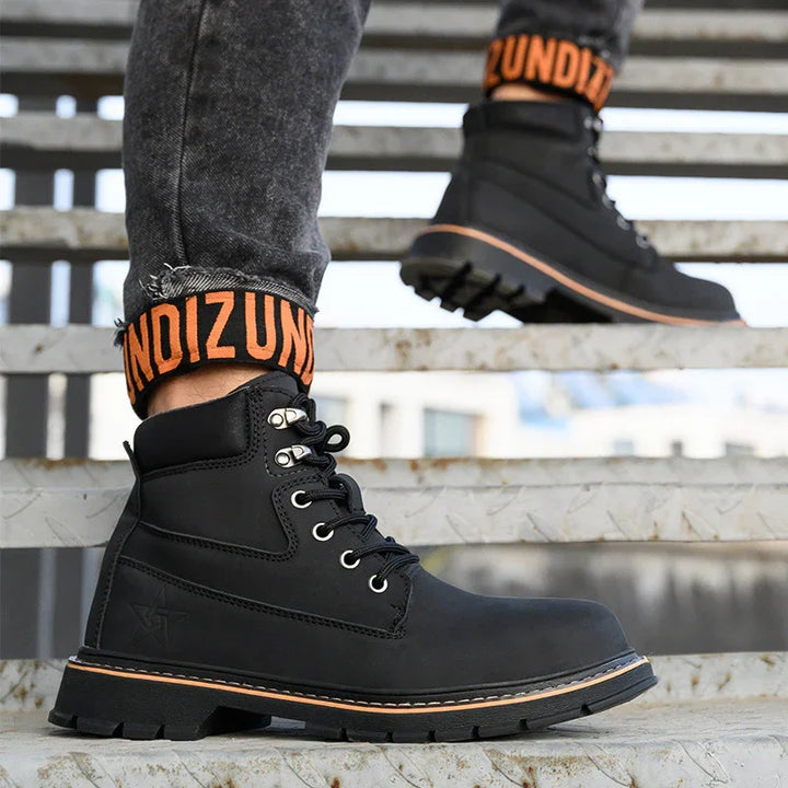 Black rugged leather boots with orange accent and black denim jeans on metal staircase
