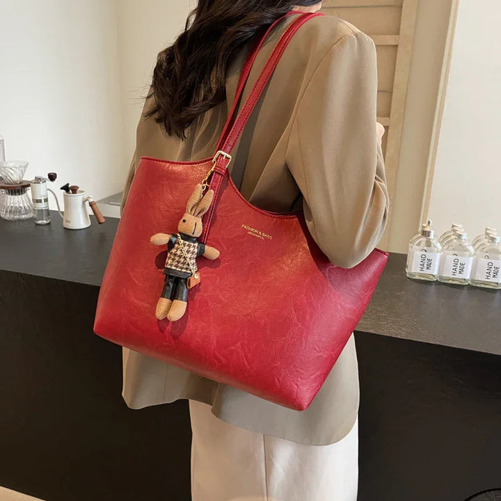 Woman carrying red leather tote bag with cute bunny keychain in modern indoor setting