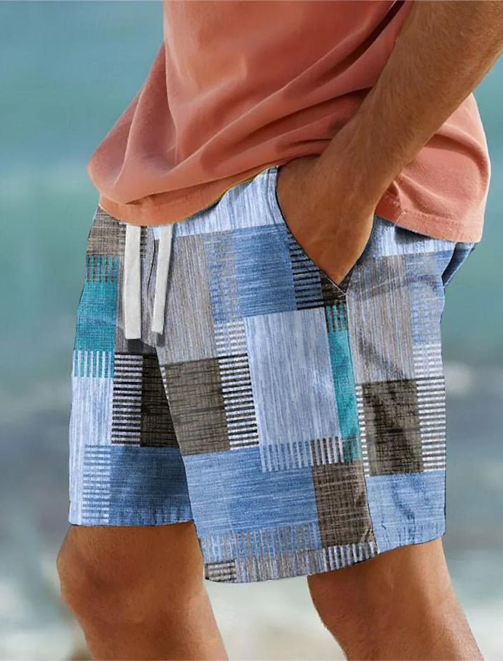 Close-up of man wearing blue and gray patchwork swim shorts with white drawstring and coral shirt at beach